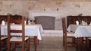 A dining area with two tables, each with a white tablecloth and wooden chairs. A stone fireplace with a white mantel is centered between the tables. - Masseria Ciavea (Gioia del Colle)