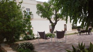 An outdoor seating area with two chairs and a table, surrounded by greenery and a building with a white facade. - Masseria Ciavea (Gioia del Colle)