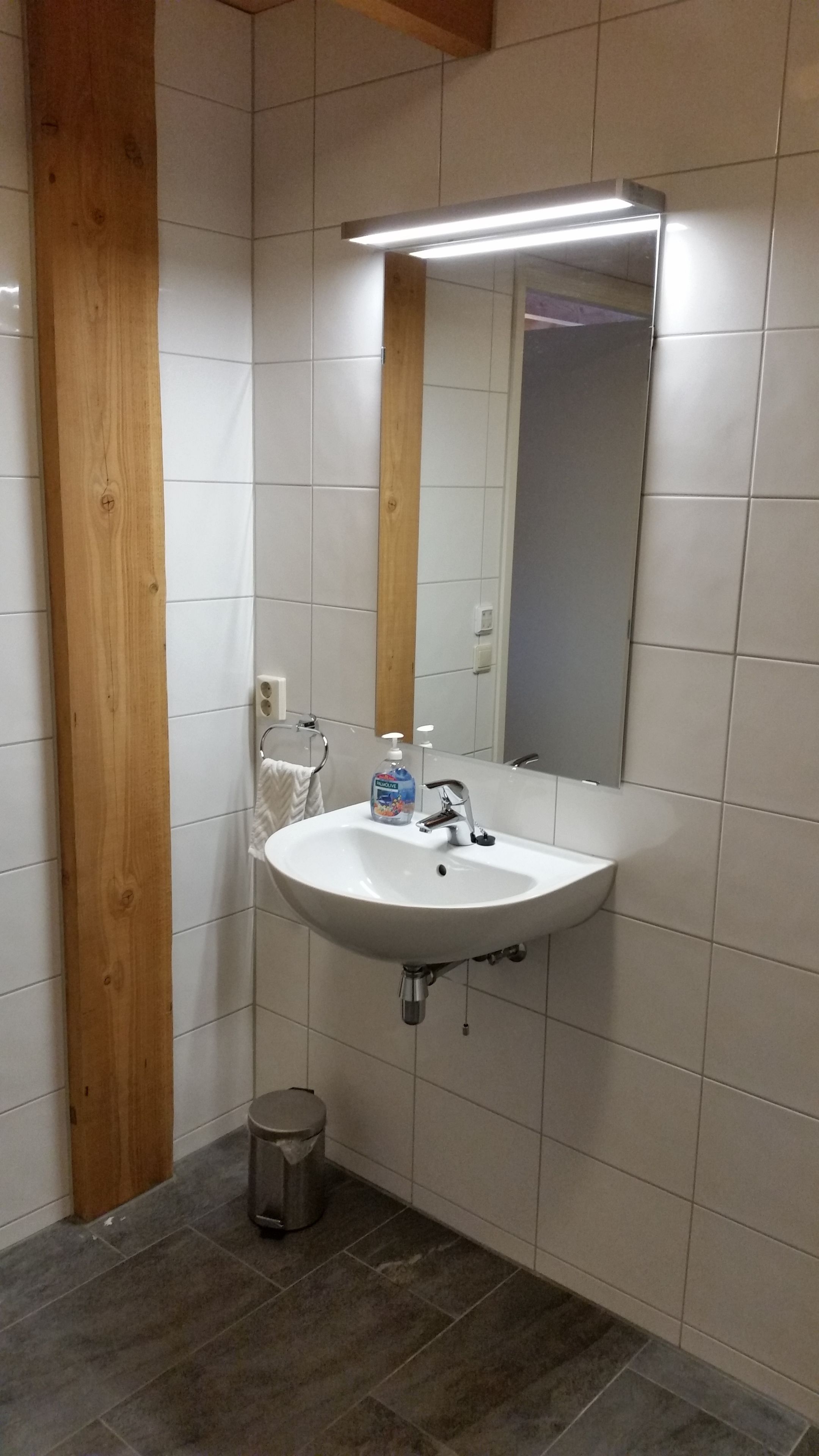 A bathroom with a white sink, a mirror, and a wooden column.