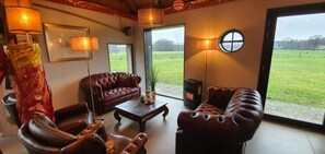 A living room with leather sofas, a coffee table, and a fireplace. There are large windows offering a view of a green field. - Roerdinkhof (Winterswijk Woold)