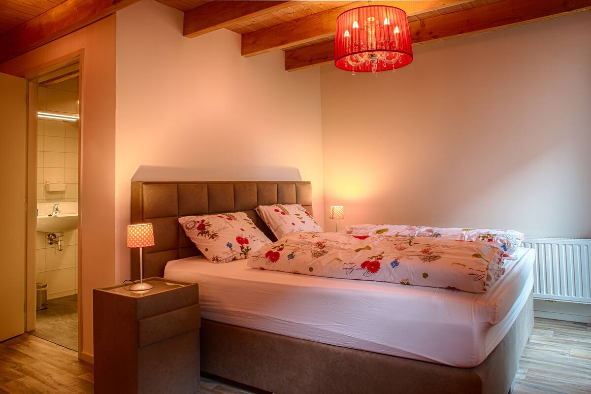 A bedroom with a bed, bedside lamps, and a wooden ceiling.