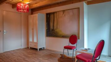 A room with wooden flooring, a red chair, a white cabinet, and a painting on the wall.