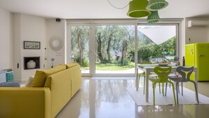 Een moderne woonkamer met een gele bank, een eethoek met tafel en stoelen, en grote schuifdeuren die uitkomen op een tuin.