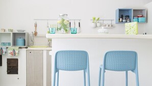 Een keuken met twee blauwe barkrukken, een hangende lamp en een wit aanrecht met diverse voorwerpen.