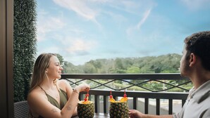 Two people sitting at a wooden table with drinks in pineapple-patterned cups, overlooking a lush green landscape. - In the heart of the city (La Fortuna)