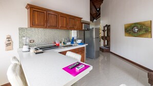 A kitchen with wooden cabinets, a stainless steel refrigerator, a microwave, and a blender on the counter. - In the heart of the city (La Fortuna)