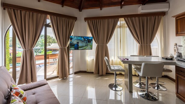 A modern living room with a large TV, a dining area, and a balcony with curtains. - In the heart of the city (La Fortuna)