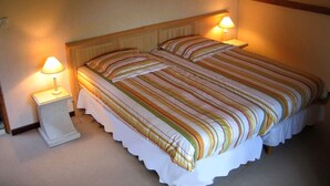A neatly made bed with striped bedding, two bedside lamps, and a framed picture on the wall. - Chambres d'Hôtes La Poirière (Brissac Loire Aubance)