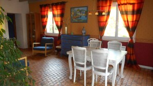 A dining area with a blue sofa, white chairs, a blue dresser, and a painting on the wall. - Chambres d'Hôtes La Poirière (Brissac Loire Aubance)