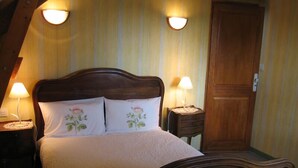 A bedroom with a wooden bed, two bedside lamps, and a wooden door. - Chambres d'Hôtes La Poirière (Brissac Loire Aubance)