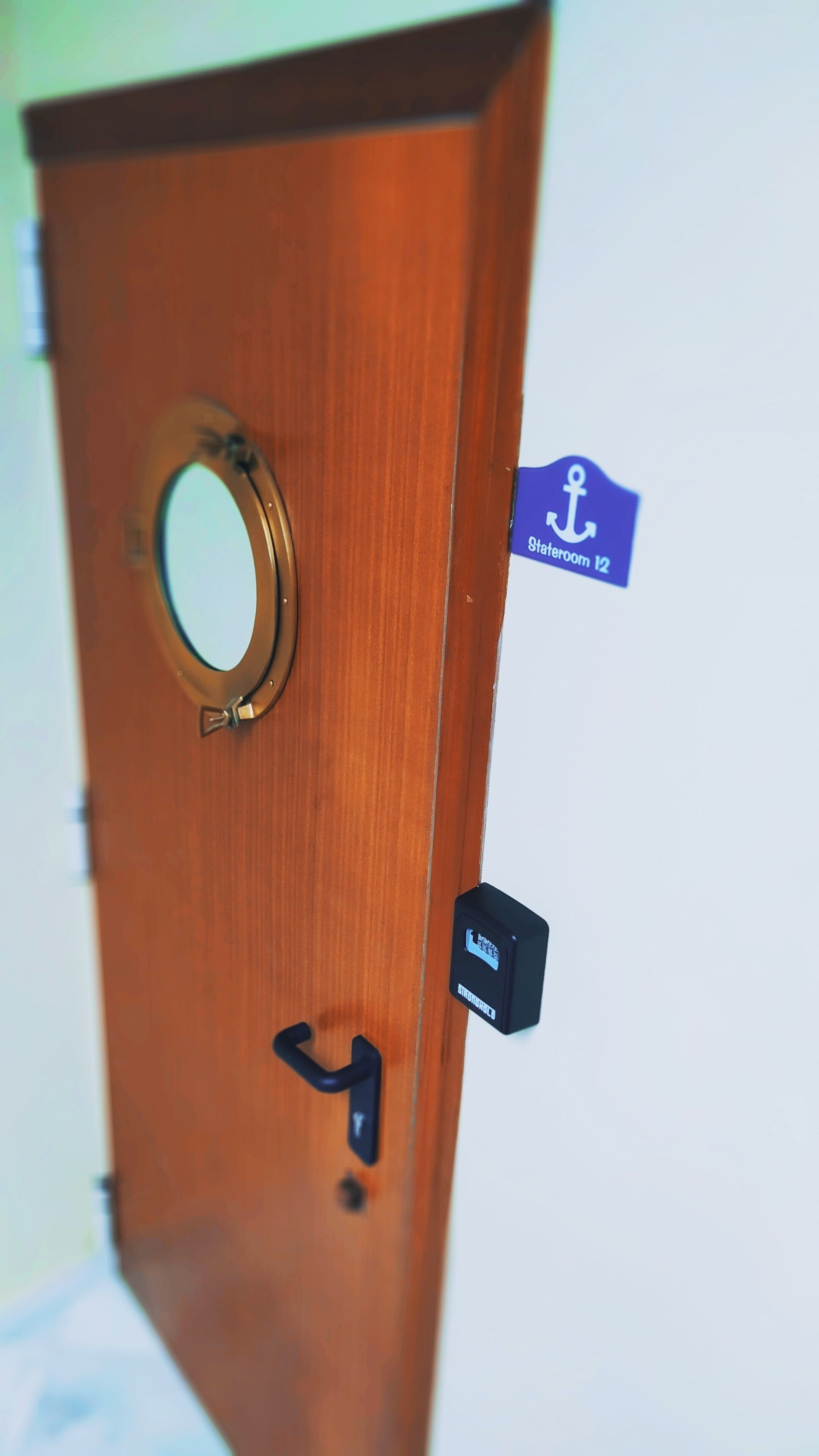 A wooden door with a circular window, a door handle, and a blue sign indicating "Stateroom 12".