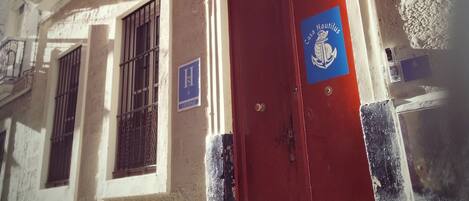A building with a red door, a blue flag with 'Casa Mauritus' text, and a balcony with a railing.