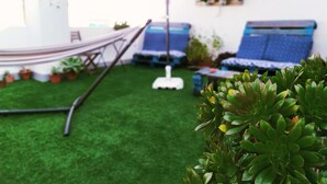 A patio with artificial grass, a hammock, two blue lounge chairs, and potted plants. - Casa Nautilus Cadiz (Cádiz)