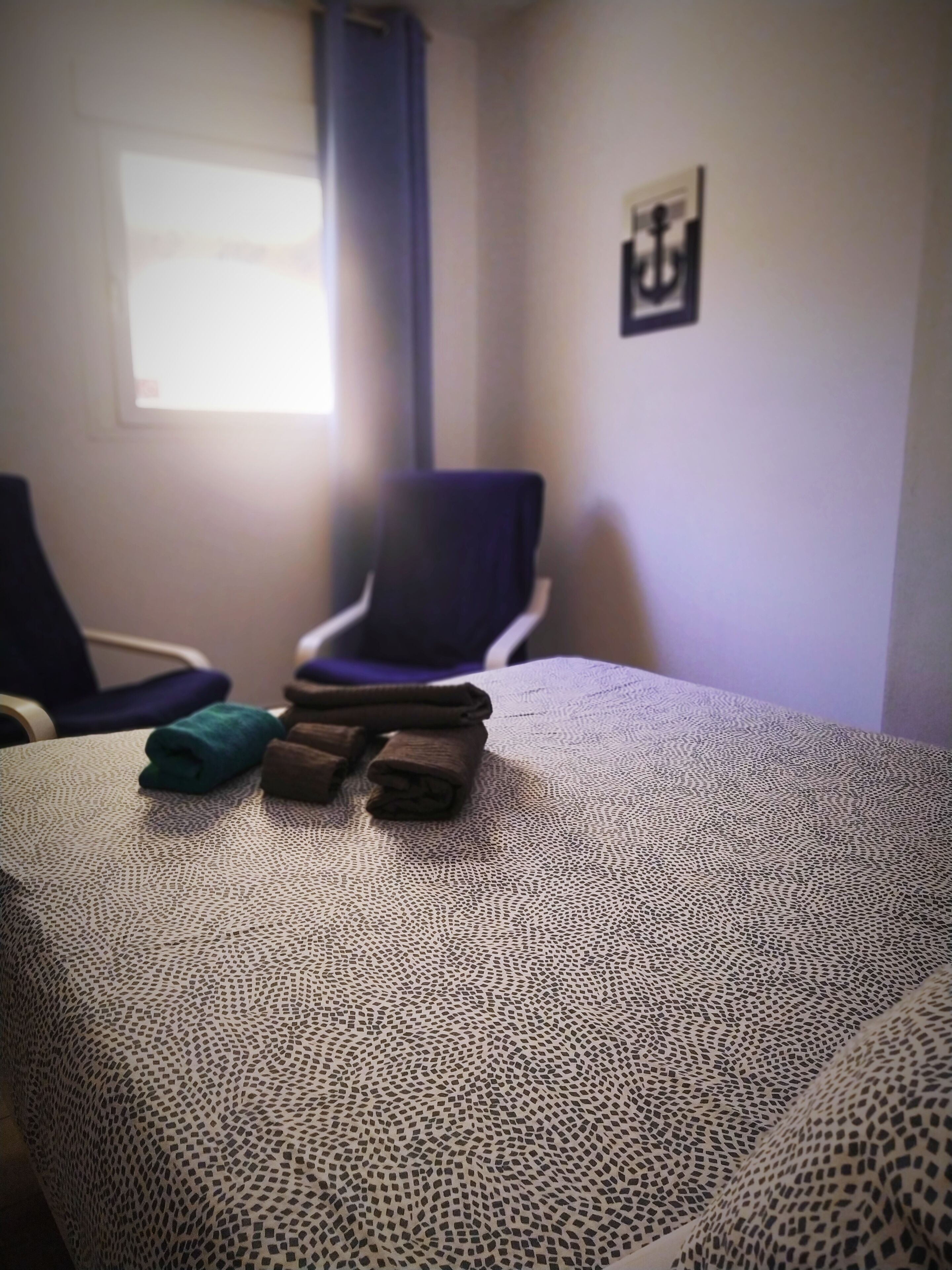 Une pièce avec une couvre-lit à motifs, une chaise et une fenêtre avec un rideau.