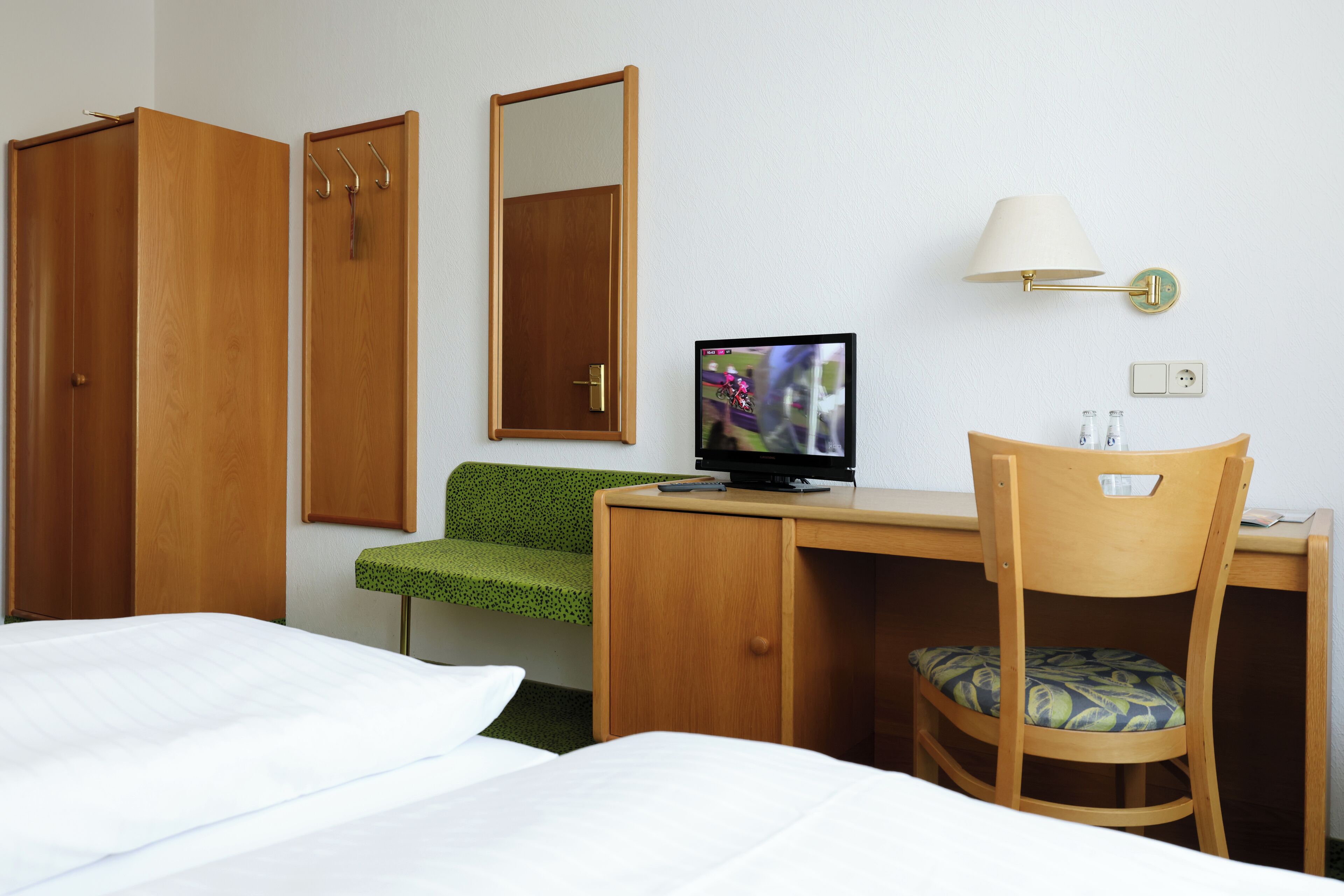 Habitación de hotel con cama, escritorio, silla, televisor y armario.