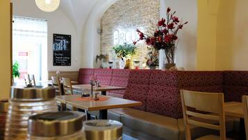 Interior de restaurante con pared de piedra, un banco de color rojo con estampado y un arreglo floral colgante.