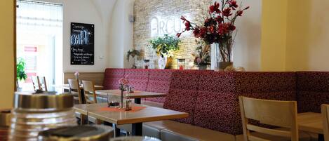 A restaurant interior with a stone wall, a red patterned bench, and a hanging flower arrangement.