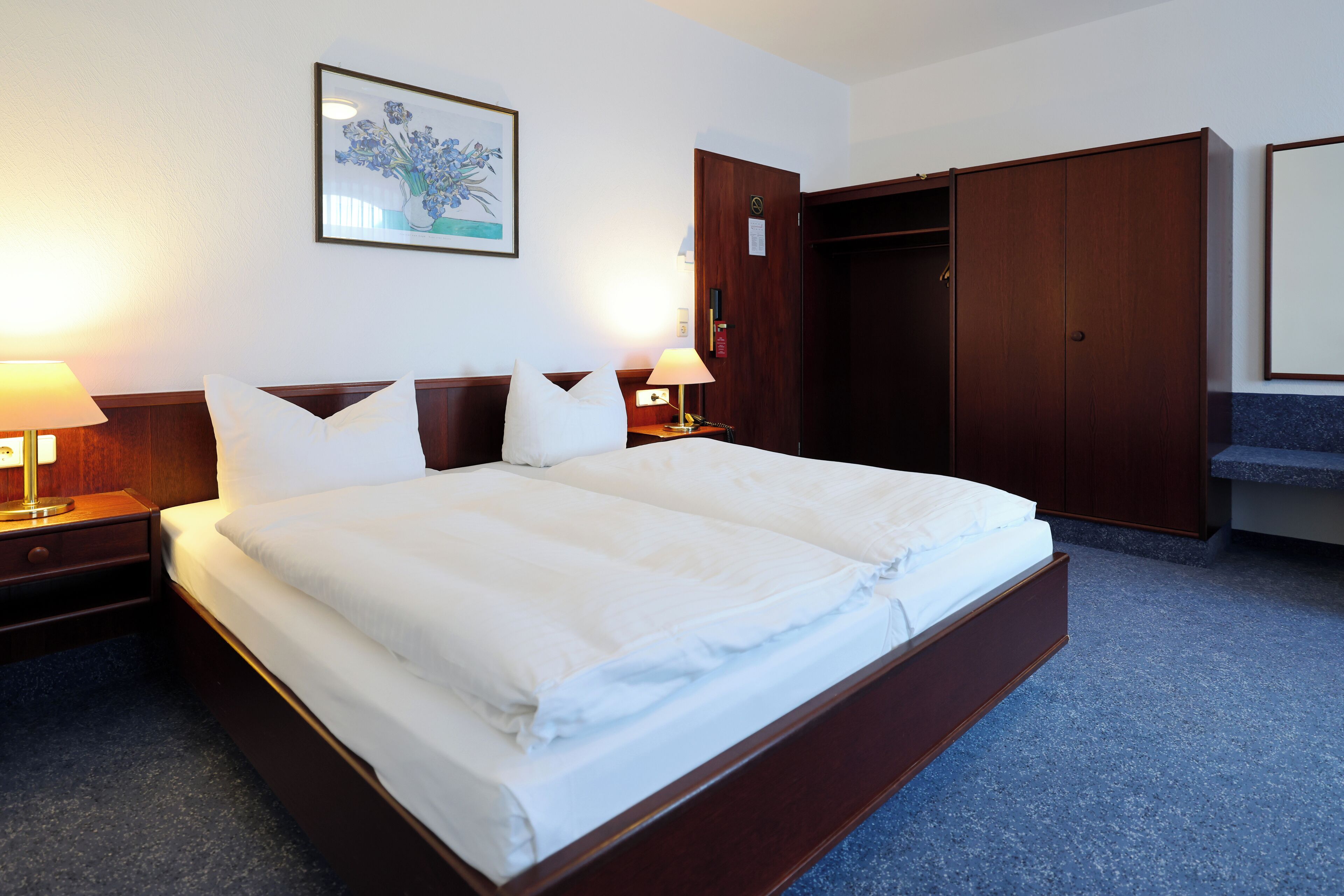 Une chambre d’hôtel avec un grand lit, deux tables de chevet avec des lampes, une armoire et un tableau encadré au mur.