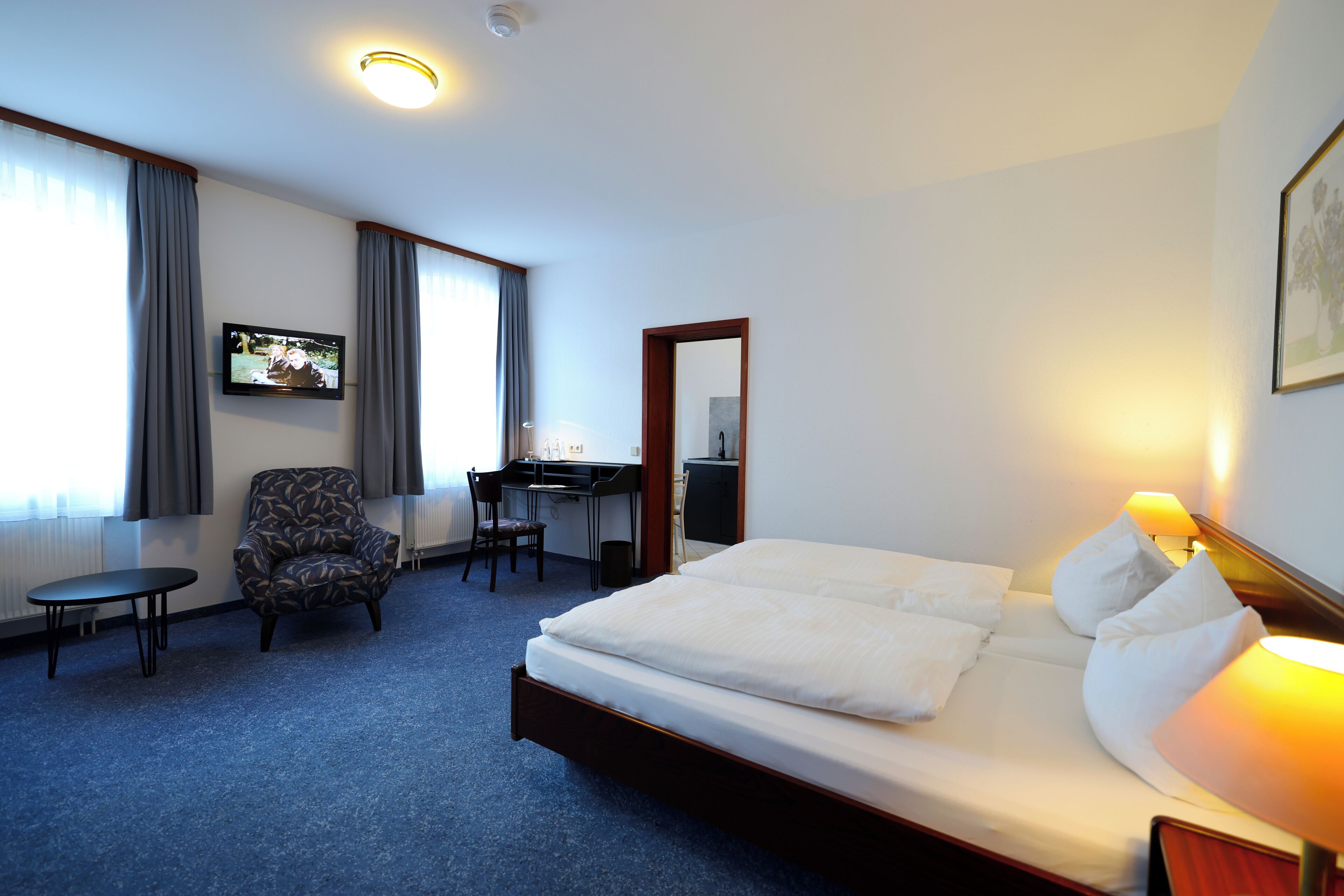 A hotel room with a bed, desk, chair, and a TV on the wall.