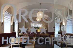 Interior de café de hotel com parede de pedra, móveis de madeira e um letreiro de neon que diz "ARCUS".