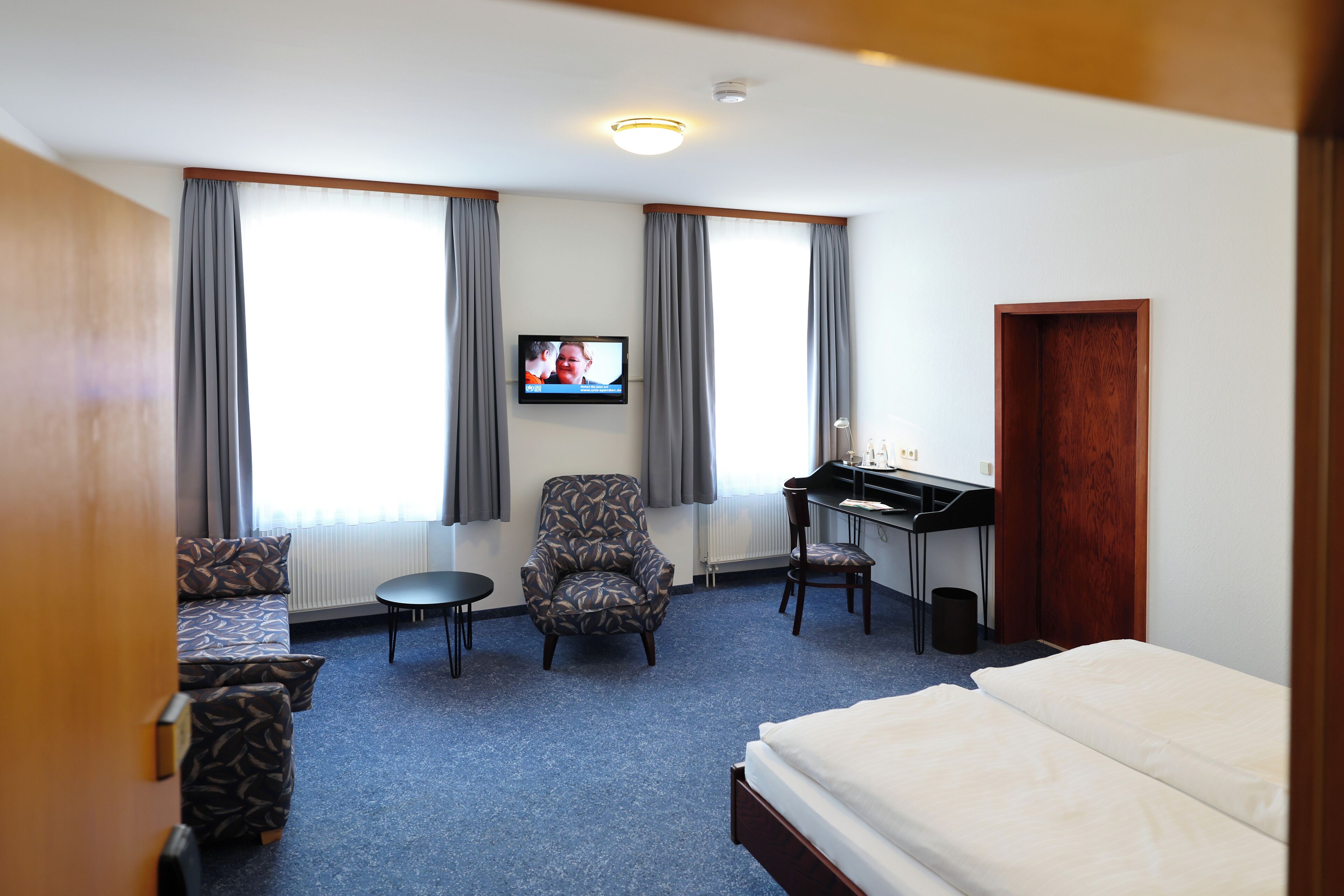 Una habitación de hotel con cama, escritorio, silla, sofá y televisor en la pared.