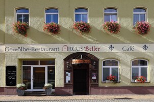 Um restaurante com uma placa indicando 'Gewölbe-Restaurant ARCUS Keller Café' e jardineiras com flores nos parapeitos das janelas.