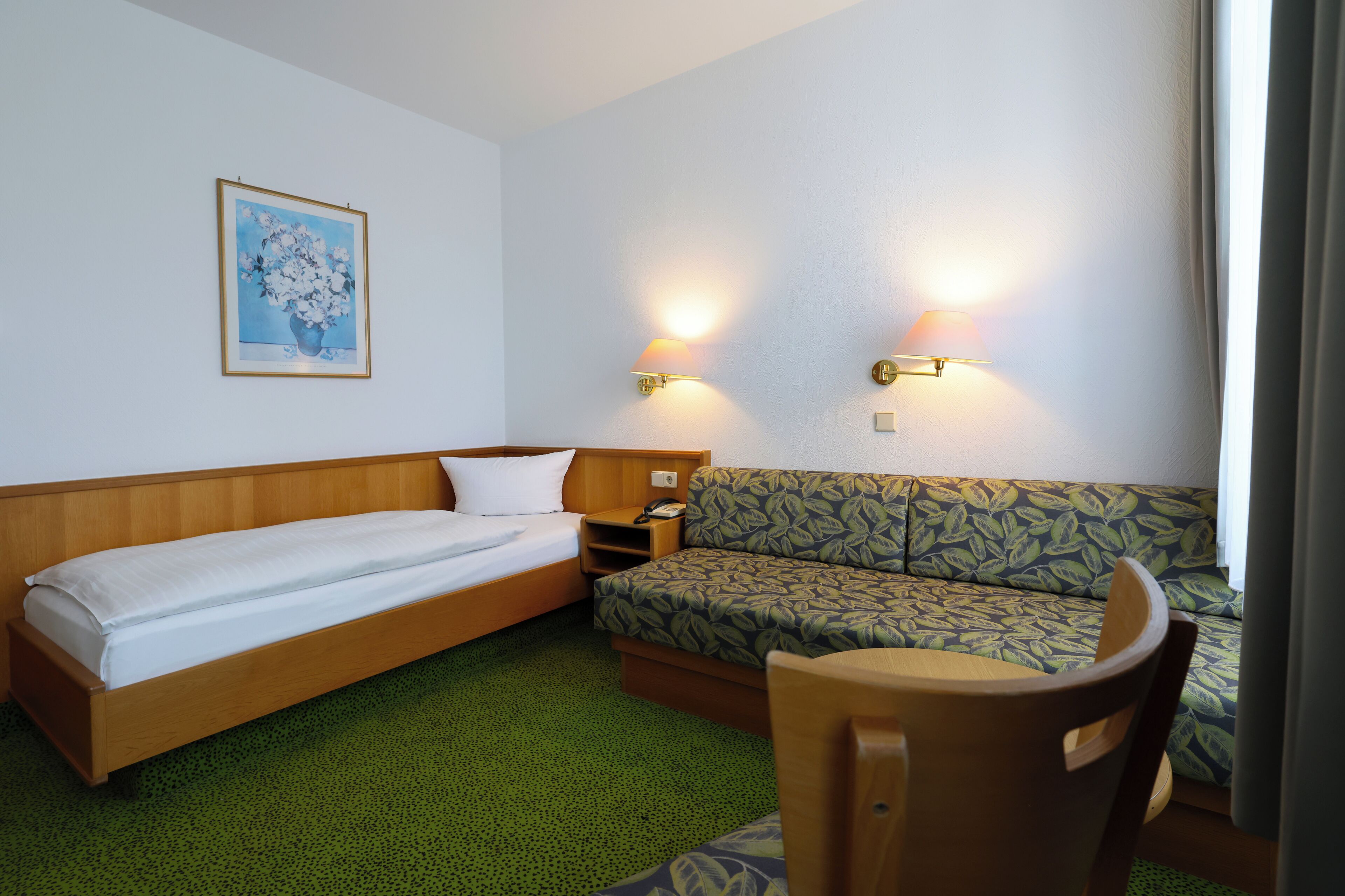 A hotel room with a single bed, a sofa, a small table, and two wall-mounted lamps.