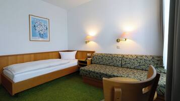 A hotel room with a single bed, a sofa, a small table, and two wall-mounted lamps.