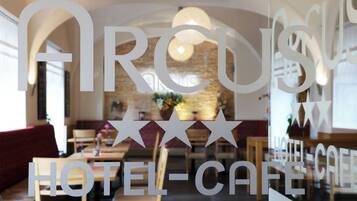 A hotel cafe interior with a stone wall, wooden furniture, and a modern chandelier.