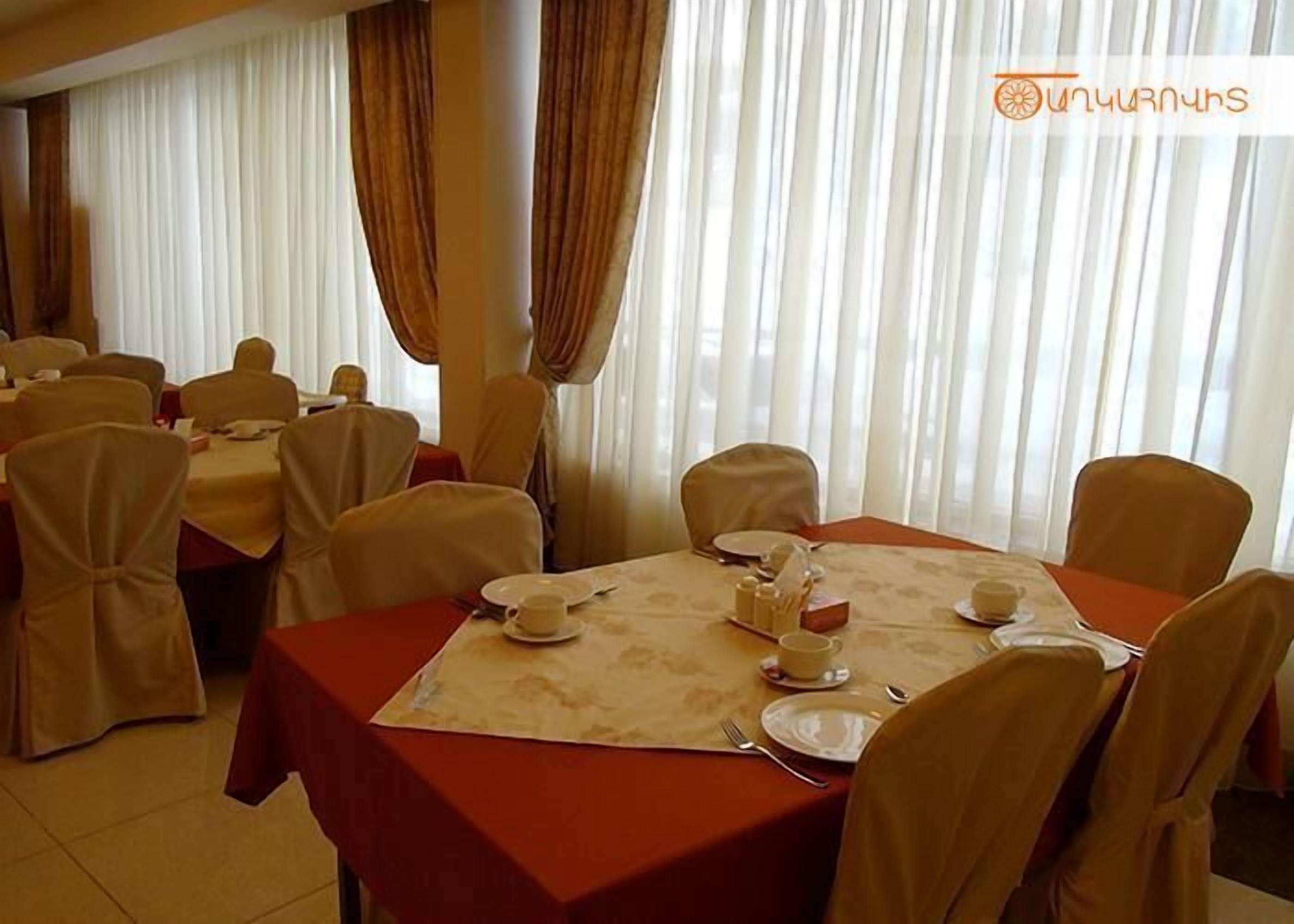 Un comedor con mesas dispuestas para una comida, con manteles blancos y sillas color beige.