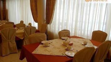 Un comedor con mesas dispuestas para una comida, con manteles blancos y sillas color beige.
