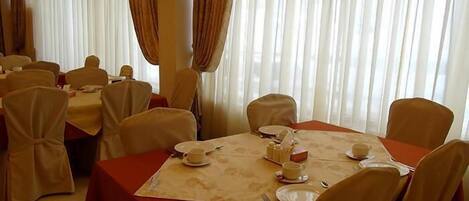 Un espace repas avec des tables dressées pour le service, agrémenté de nappes blanches et de chaises beiges.
