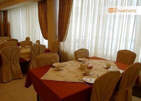 Un comedor con mesas dispuestas para una comida, con manteles blancos y sillas color beige.