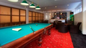 A pool table with green felt, surrounded by brown chairs, in a room with a red carpet and wooden panel walls. - Tsaghkahovit (Tsaghkadzor)