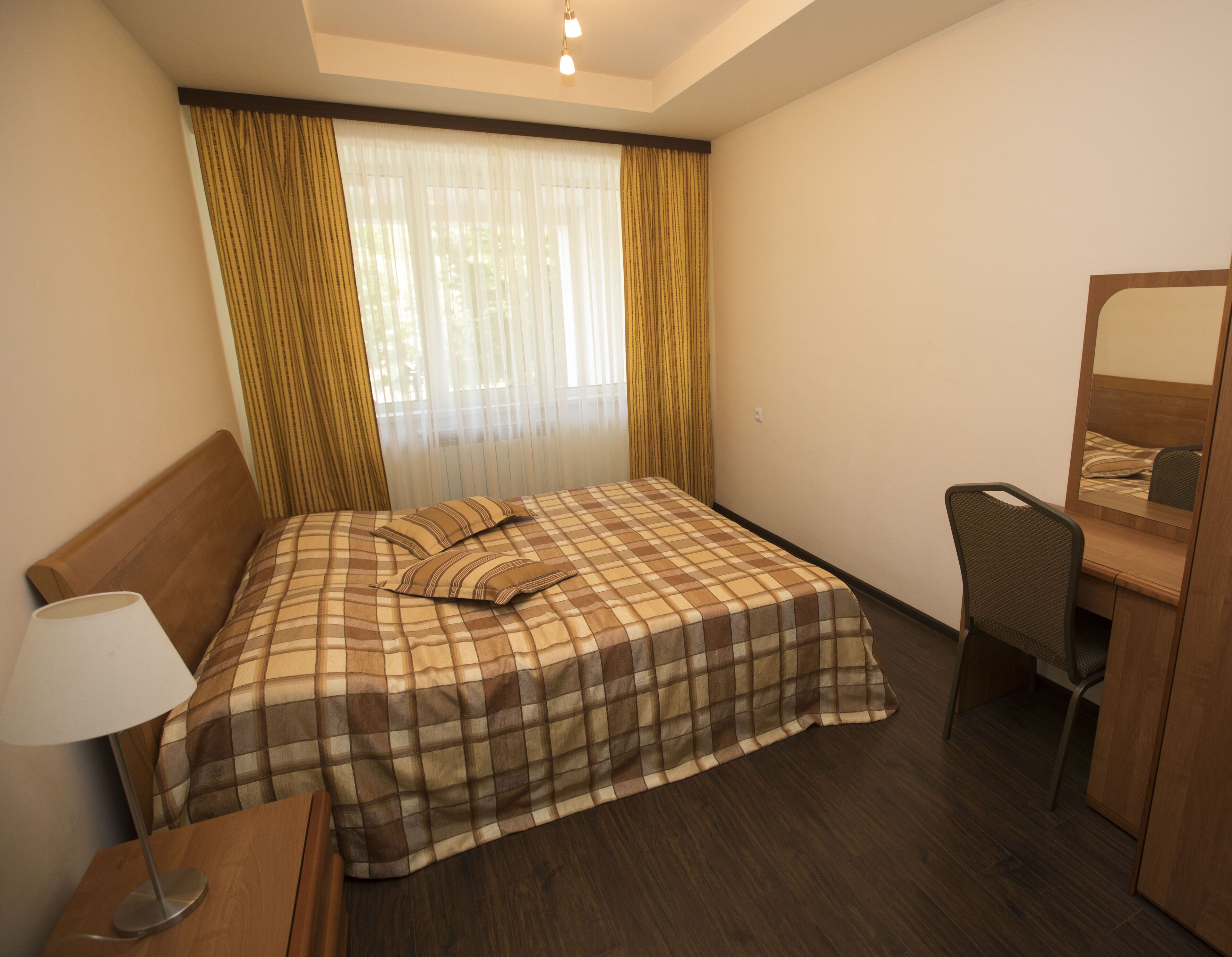 A hotel room with a bed, a desk, a chair, a lamp, and a window with curtains.