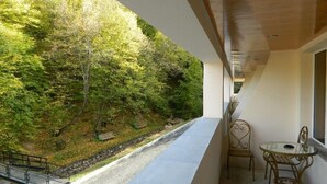 A balcony with a view of a forested hillside, a small table, and a chair. - Tsaghkahovit (Tsaghkadzor)