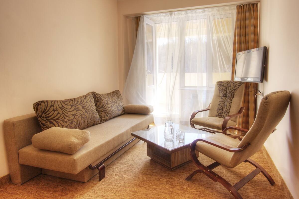 A living room with a sofa, armchair, coffee table, and a flat-screen TV mounted on the wall.