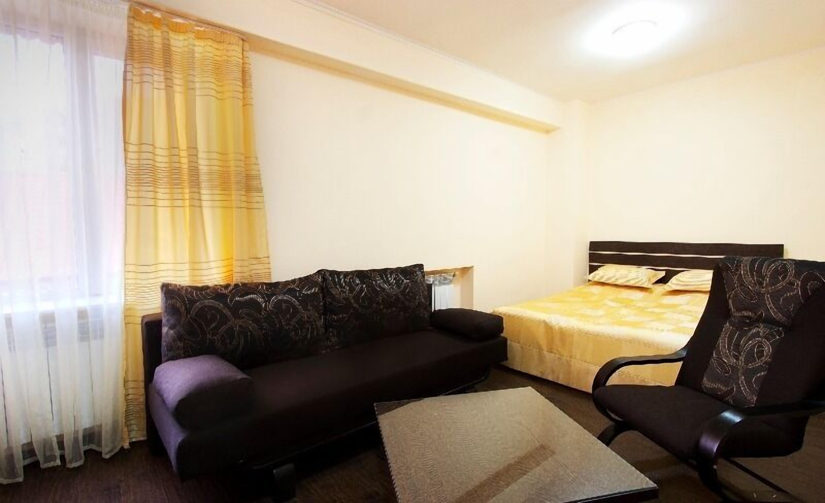 A small, well-lit room with a bed, a sofa, and a chair.