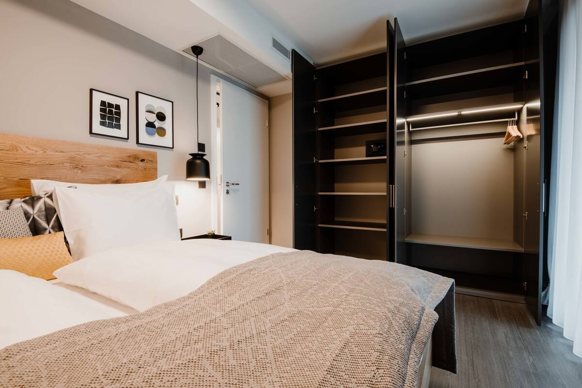 Un dormitorio moderno con una cama grande, cabecera de madera, una mesita de noche y un vestidor con espacio para colgar ropa.