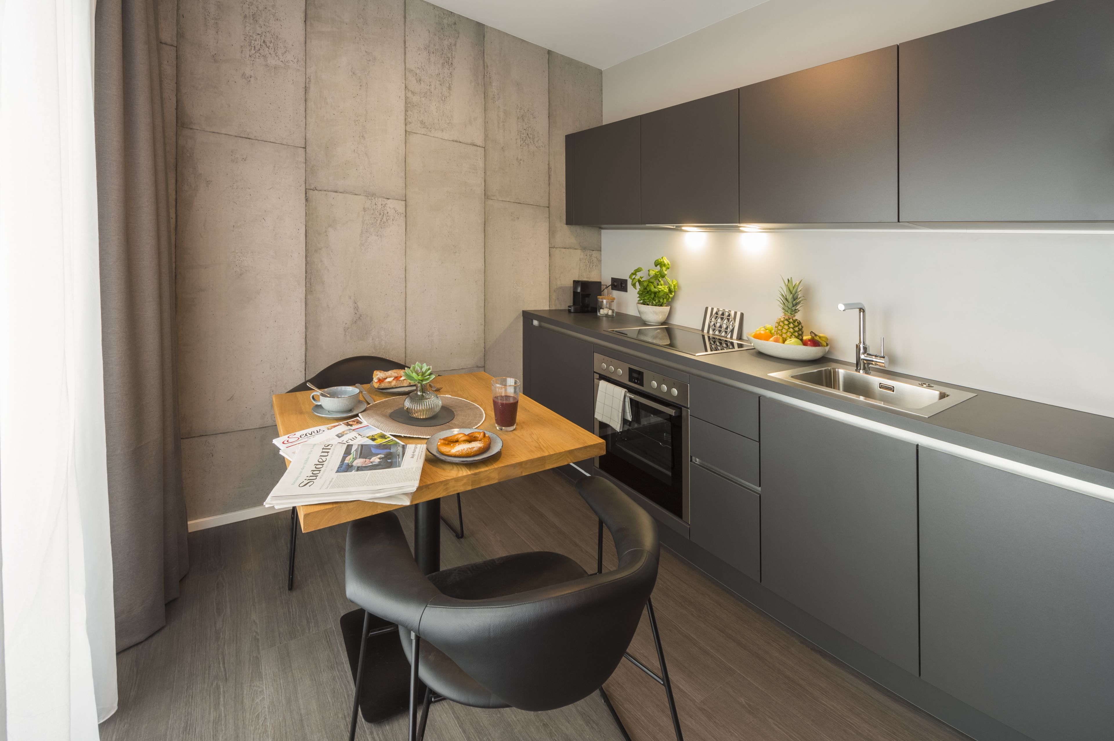 A modern kitchen with grey cabinets, a wooden dining table, and a black chair.