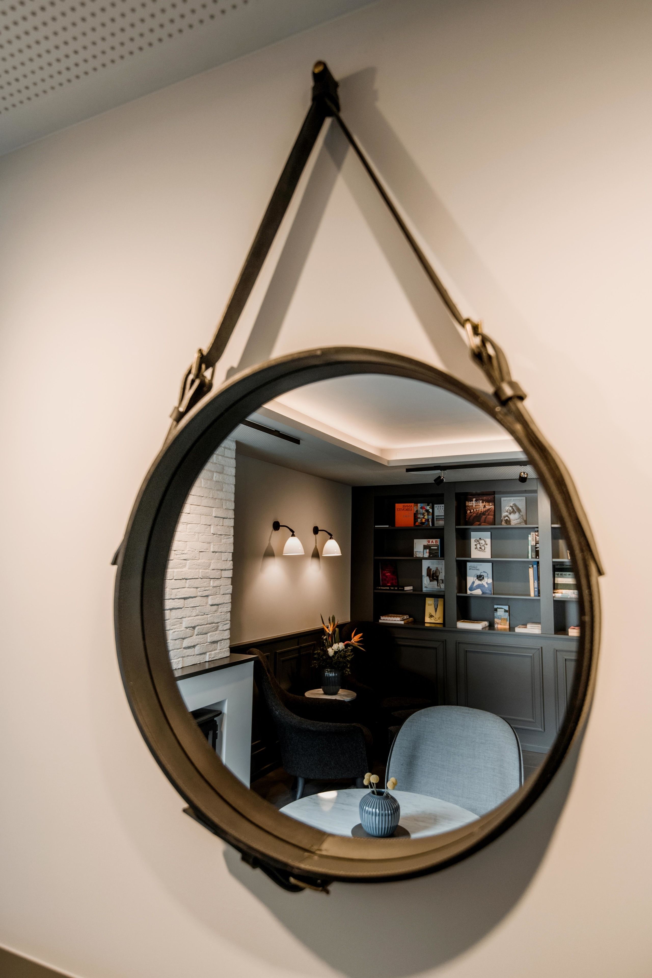 Un grand miroir rond suspendu au plafond, qui reflète une pièce avec un mur en briques, une bibliothèque et un coin repas comprenant une table et des chaises.