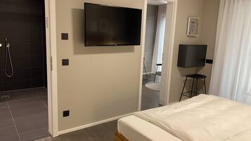 A hotel room with a bed, a TV mounted on the wall, a shower area, and a door leading to a bathroom.