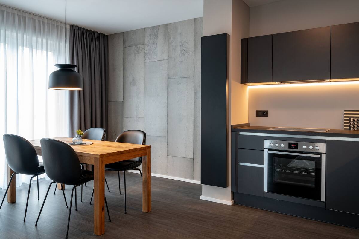 Una cocina moderna con horno empotrado, comedor con mesa de madera y sillas negras, e iluminación colgante.