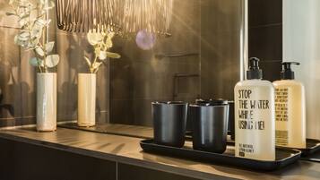 A bathroom vanity with a mirror, two vases with plants, a tray with two black cups, and two bottles of soap.