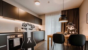 A modern kitchen with dark cabinetry, a built-in oven, and a dining area with a wooden table and black chairs.