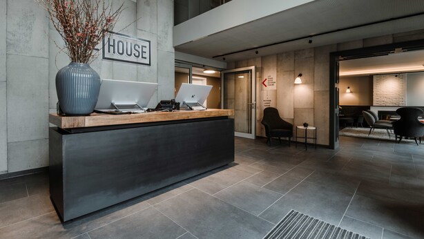 A reception desk with a laptop, a vase with branches, and a sign that reads "HOUSE".