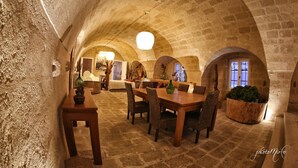 A dining area with a high arched ceiling, stone walls, and a round table with chairs. - Domus Decclesiis (Gravina in Puglia)