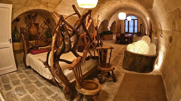A rustic room with a bed, wooden chairs, a table, and a large lamp. - Domus Decclesiis (Gravina in Puglia)