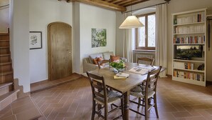 A dining area with a wooden table, chairs, a hanging lamp, a bookshelf, and a window with curtains. - Luxury Chianti in Olives in Panzano Chianti (Panzano)