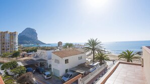A coastal residential area with a prominent cliff, a beach, and a white building with a tiled roof. - Apartment Arenal 4 - PlusHolidays (Calpe)